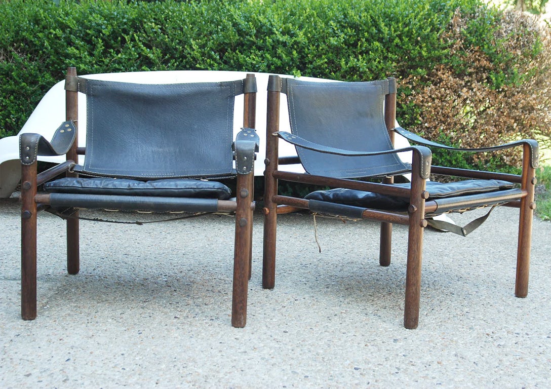 A pair of Arne Norell  black leather chairs with sling seats and arms over a wooden frame.