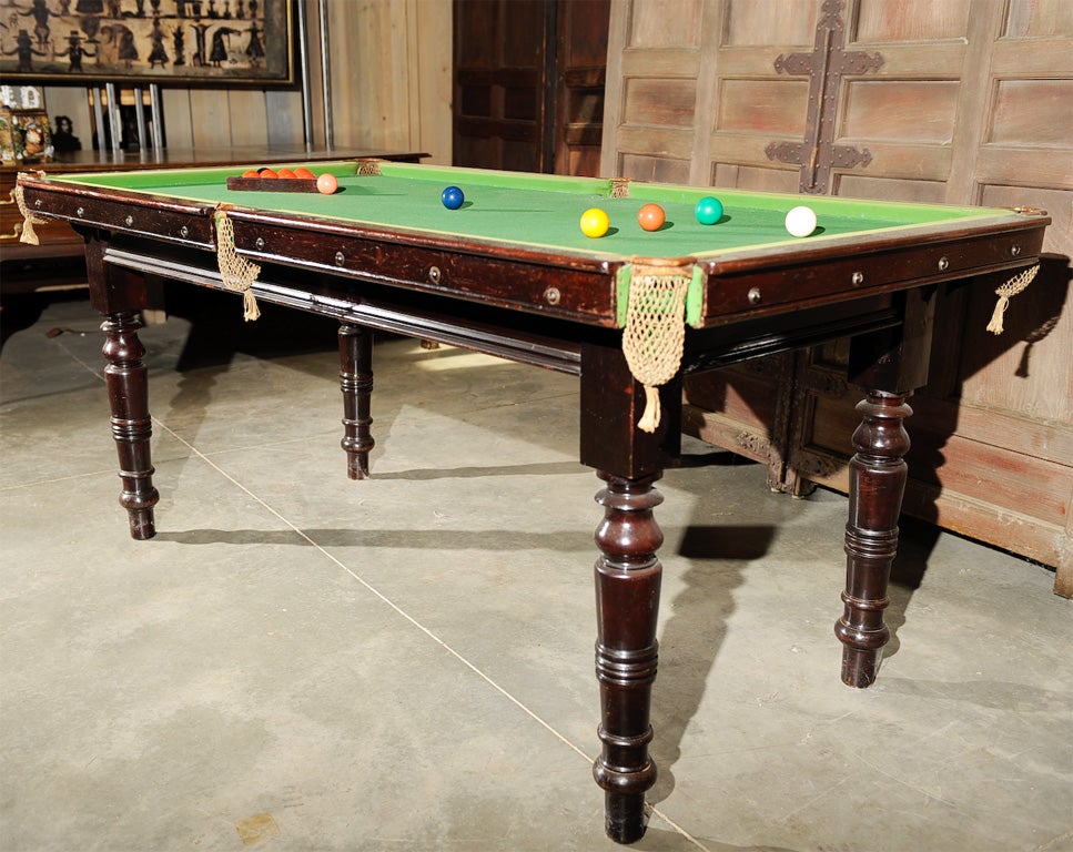 An antique English snooker table with accessories(balls, rack, scoring chart, bridges, cues). Green felt top with string pockets