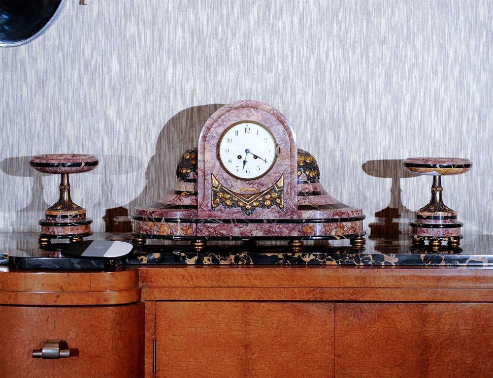 French period Art Deco three-piece mantle clock set. Clock and tazza-shaped garniture composed of two-tone layered marble with bronze mounts. Previouly reconditioned, includes pendulum, bell and key.