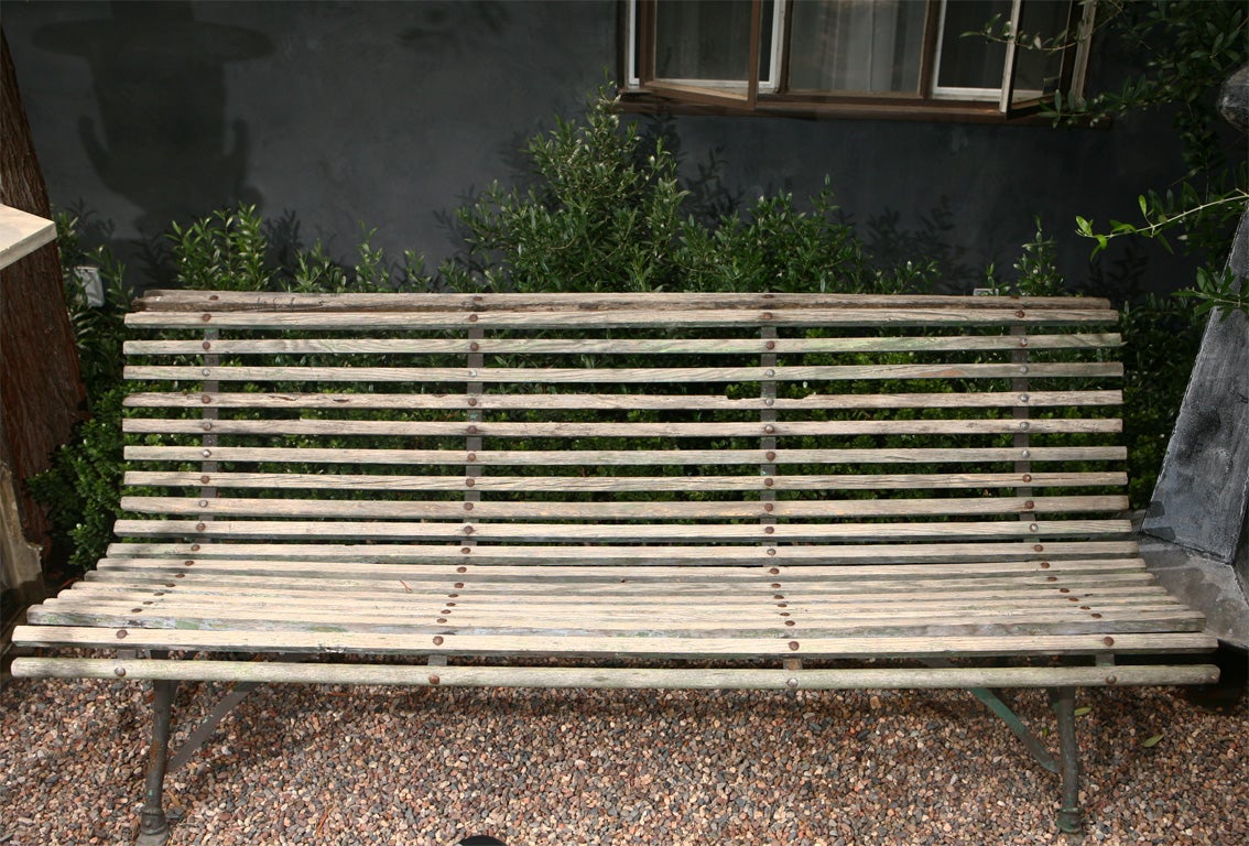 An English 19th century garden bench with wood slat curved back and seat  raised on curved iron stretchers and  legs and with elegant hoof feet.