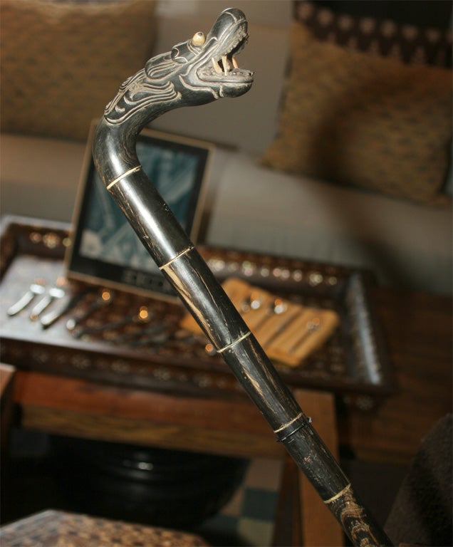 A cane or walking stick with carved serpent head and inlaid eyes and rings on shaft, on stand.  Two available: a 33
