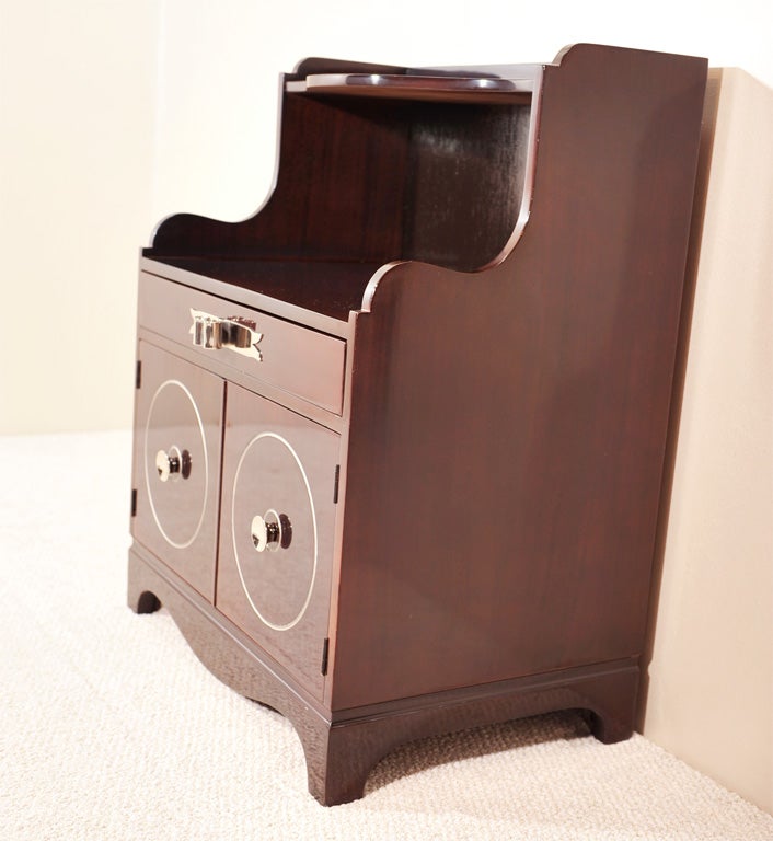 Exceptional pair of one-drawer ebonized mahogany night stands with polished nickel stylized ribbon hardware with incised circular silver leaf details on front doors.