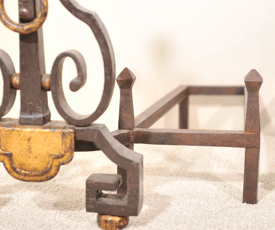Exceptional pair of hand-forged wrought iron andirons with gilt iron details and attached log holder. Overall width is 34.5 inches. 