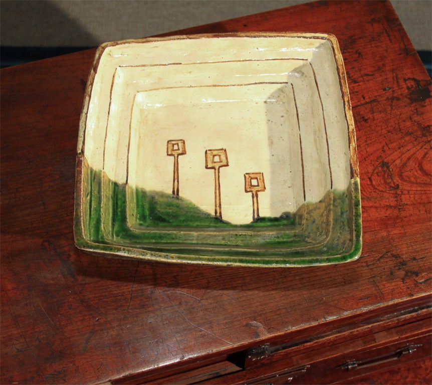 Japanese square oribe ware dish with high, irregular stepped sides. Pleasingly decorated with an abstract design of three army standards seen beyond a field of green.