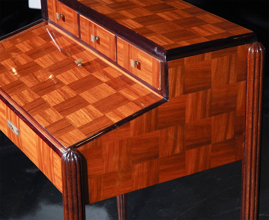 Writing table attributed to Maurice Dufrene in rosewood and mahogany marquetry with carved legs. Three small drawers and fold out writing surface with original embossed leather. Original condition.