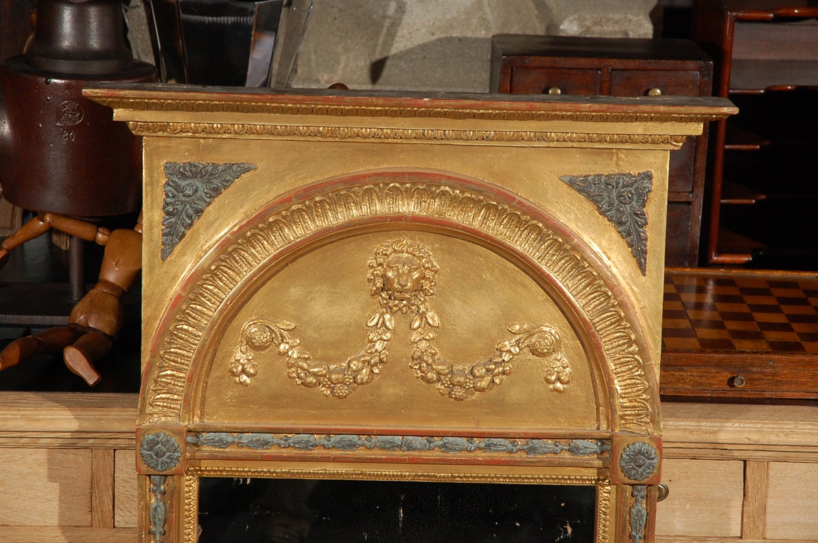 A rectangular gilt mirror with cornice top over a carved arch with a carved lion's head guarding fruit swags. The lower mirror with carved neoclassical motifs and anthemion in bottom reserve, circa 1800.