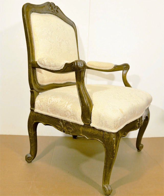 WITH CARTOUCHE-SHAPED BACKREST AND SERPENTINE FRONTED SEAT, THE PADDED ARMRESTS RAISED ON VOLUTED SUPPORTS, RAISED ON CABRIOLE LEGS ENDING IN VOLUTED TOES, THE RAILS AND LEGS CARVED WITH LEAF TIP MOTIFS, WITH LOOSE BACK CUSHION.