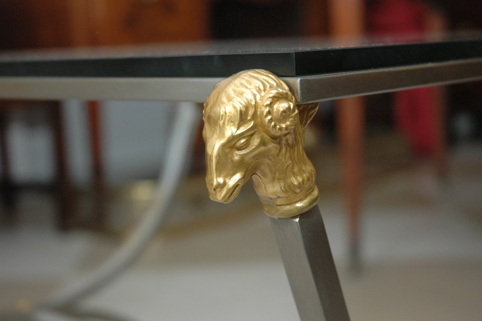 French bronze and steel ram's head table with glass top, having a polished steel classical style frame with bronze ram's heads in each corner and ram's feet at the base of the legs.