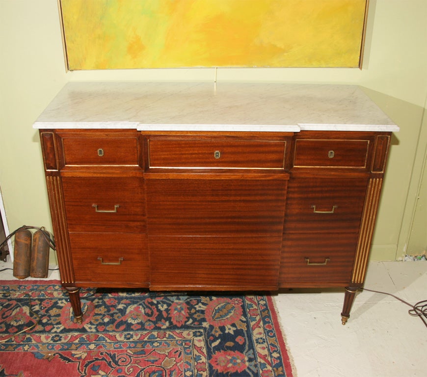 Marble top commode stamped Jansen with fluted legs with gild highlights and bronze accents.