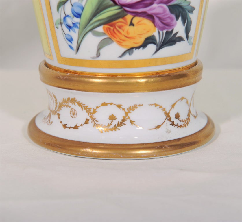 A pair of cache pots and stands on a yellow ground feature a panel with hand painted tulips, roses and blue bells surrounded by lush gilding.