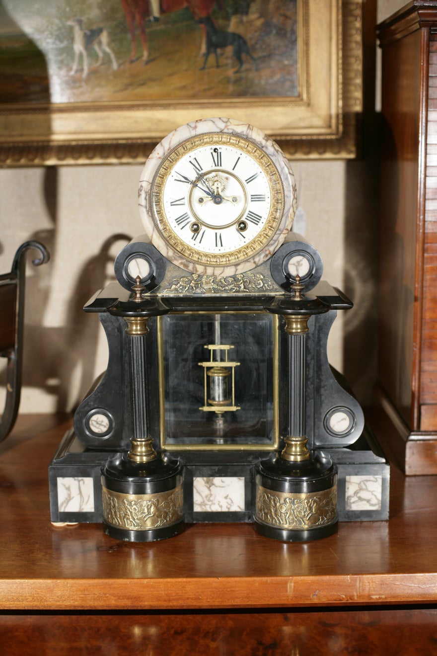 French, black marble mantel clock with enamel face having brass surround. Narrow columns lead to heavy brass pediments with relief work depicting classical Greek army.