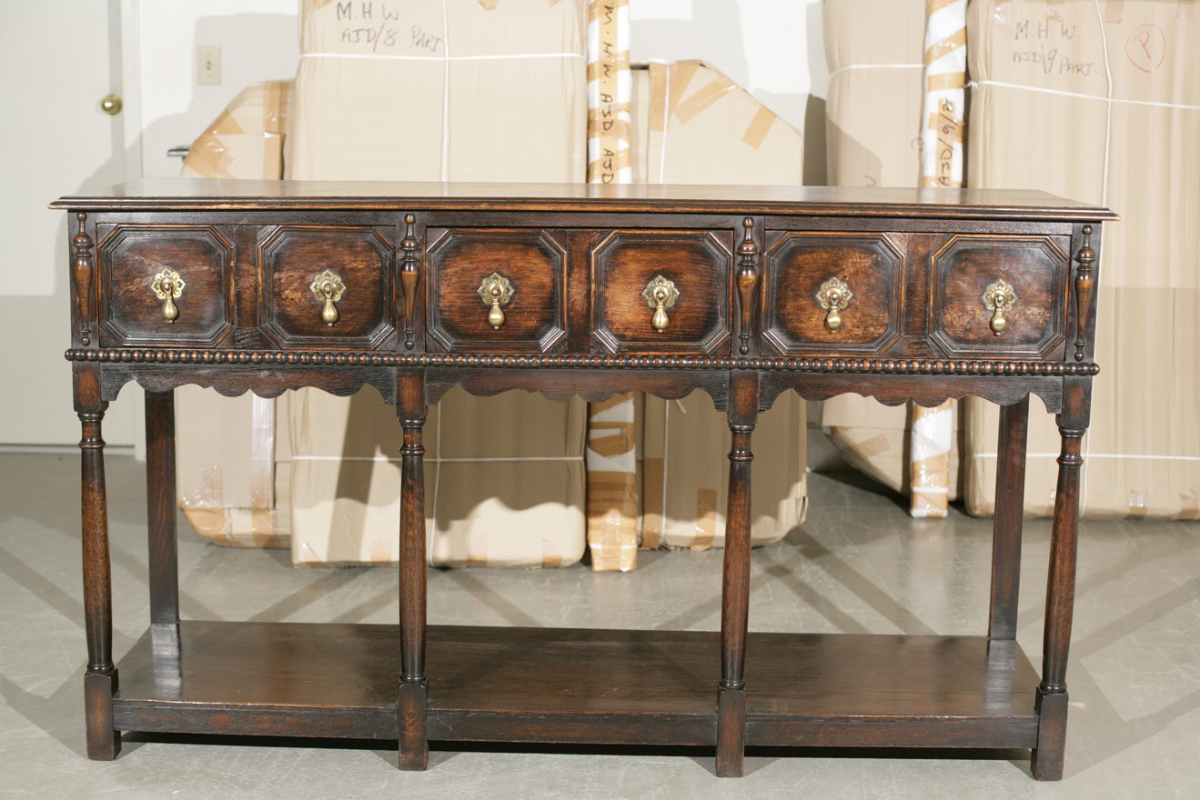 English, oak, Jacobean Revival potboard server with three drawers.  Deeply paneled drawer fronts over scalloped apron and gun barrel turned legs leading to the potboard base are consistent with the style.  Heavy solid brass teardrop drawer pulls