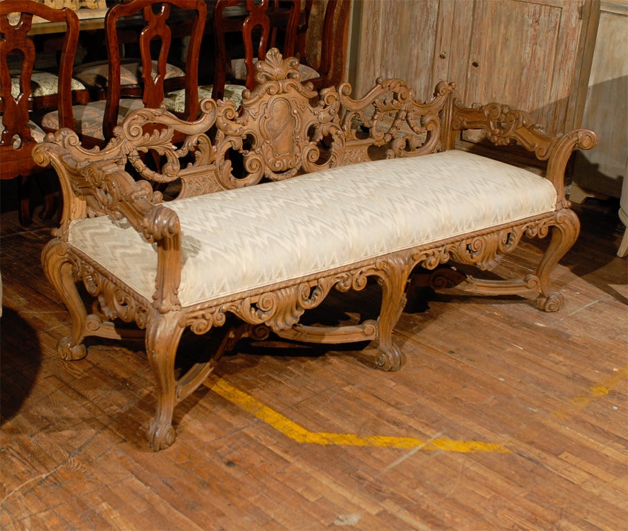 An exquisite, richly carved Italian wooden bench with upholstered seat, cabriole legs and gorgeous cross stretcher.