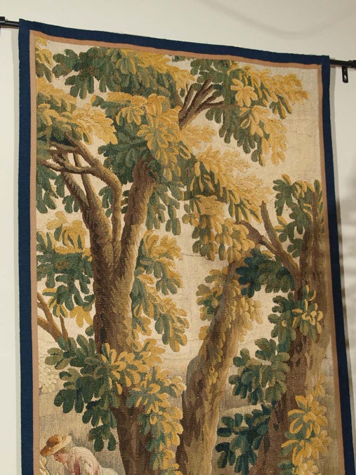 Aubusson tapestry in shades of brown, beige, blue, gold and red depicting a pleasing pastoral scene including forest, meadows, flowers and a woman harvesting grain.
