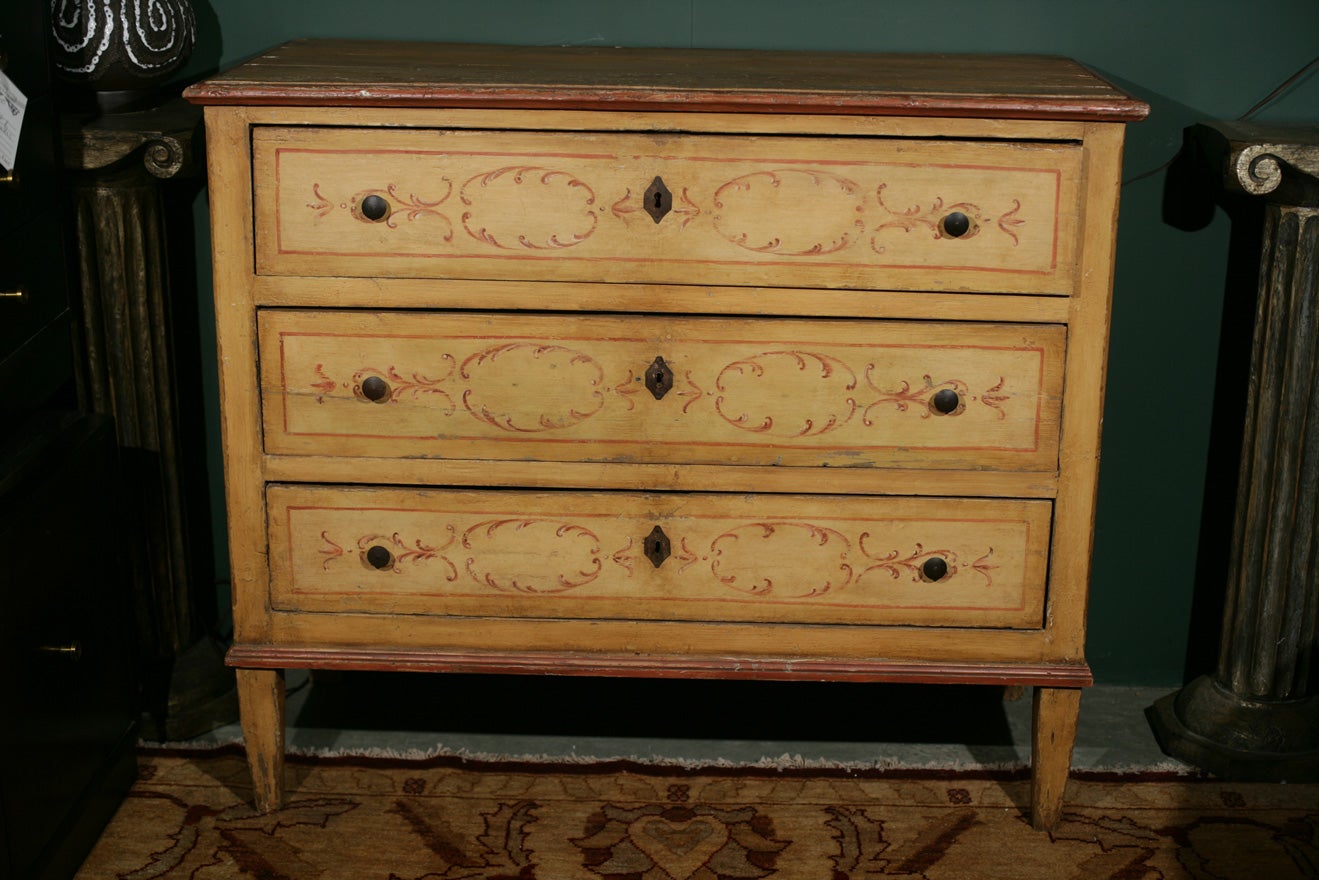 A beautifully distressed yellow and red painted French provincial dresser with three drawers, standing on squared tapering feet.