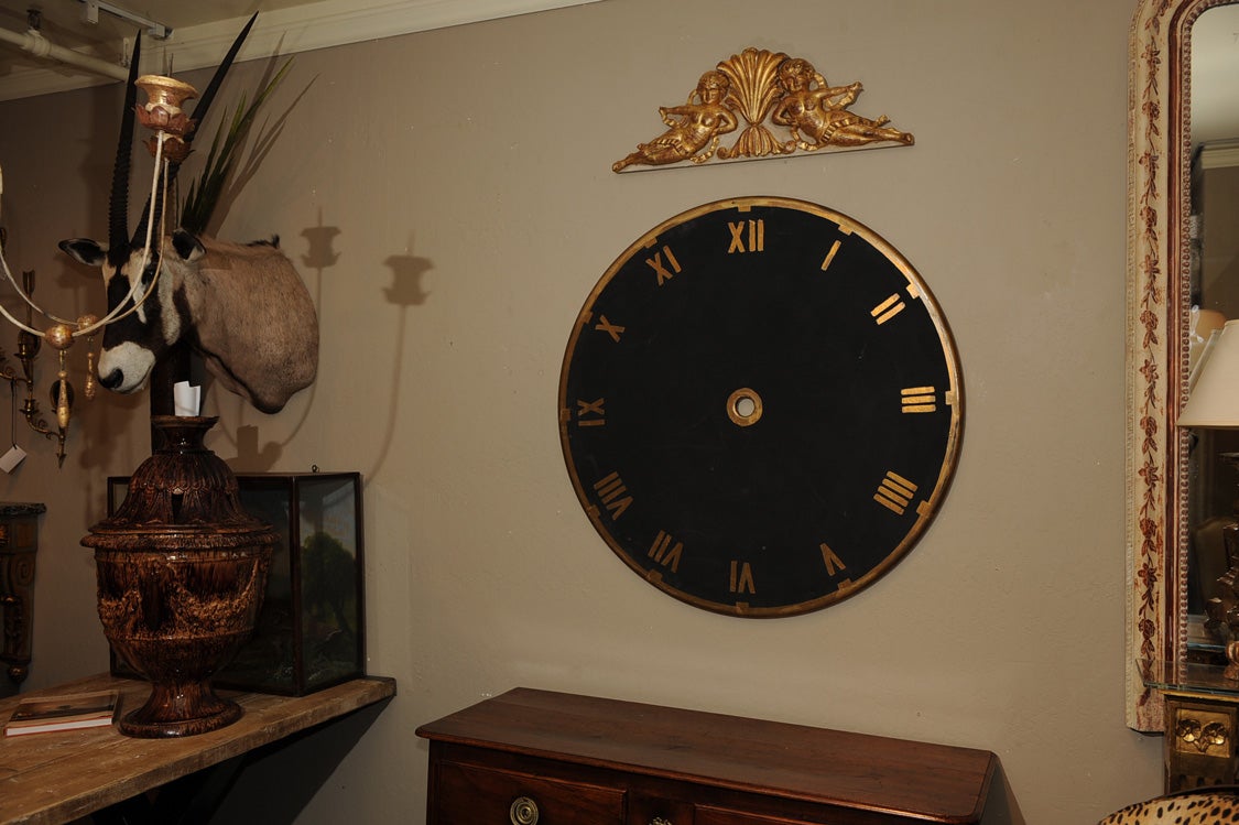 The large ebonized and parcel gilt turret clock dial (sans hands) with a chapter ring of elegant gilt Roman numerals and hour markers.