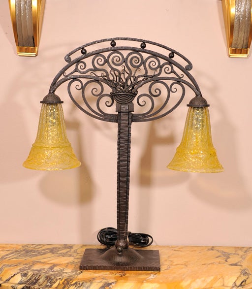 French Art Deco double-armed table lamp in wrought iron, with two yellow acid-etched glass shades, from circa 1925. Iron base numbered and stamped with indistinct signature and shades signed Daum Nancy with cross of Lorraine.
