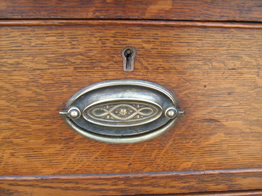 Antique oak wood chest of five drawers with decorative oval hardware.