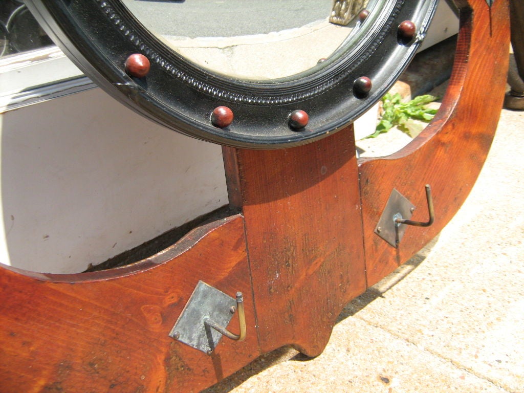 Round convex mirror attached to anchor shape wooden coatrack with five metal hooks.