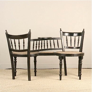 Anglo-Indian solid ebony tete-a-tete style chair with cane seats. Spindle turned backs and center connecting arch. Rear legs are straight with tapered profile. Front legs are turned. Oval shaped center table.