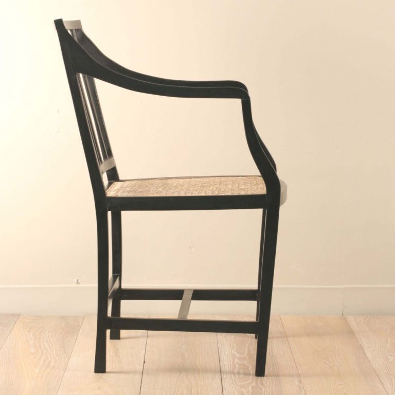 Very elegant and simple solid ebony armchair. Downward curving arms in a thin profile have a slight concave trough carved the length of the arm. Rear splats are slightly tapered. Chair rails, splines and legs have the same thin profile. Newly caned