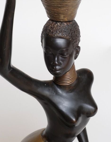 The sensual undulating form of a woman in kneeling position with right hand raised to steady the trumpet-shaped basket on her head while her upper body is turned dramatically to the right; the serene face is well-deliniated; with various portions in