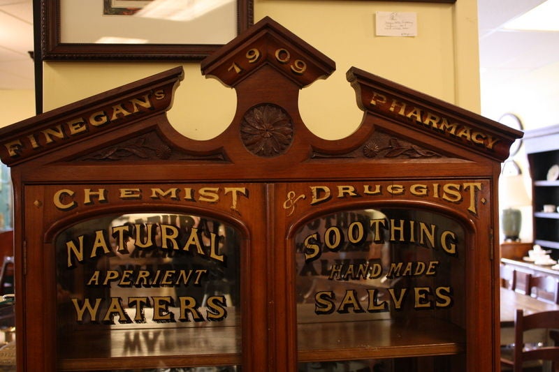 An antique mahogany display cabinet from England with new decorative pharmacy painting. PERFUME, COLOGNES, SALVES, SALTS, WATERS, BRUSHES, HAIR LOTIONS. Unique and Fun, great for the Bathroom or Dressing Room, or anywhere. Pretty floral carving on