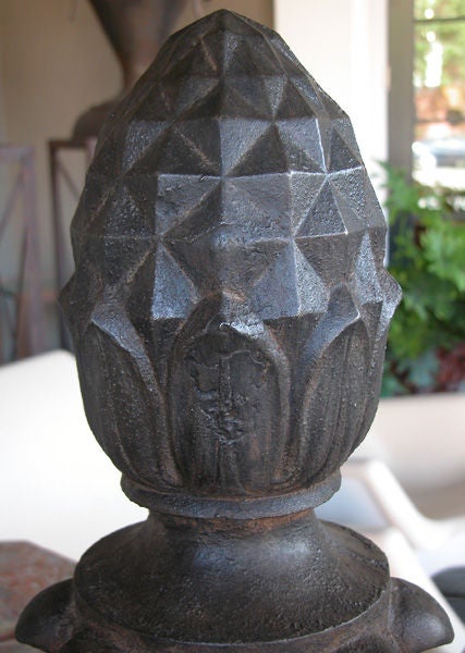 A handsome pair of American cast iron pineapple-form finials; each surmounted by a stylized pineapple above a mid-section of outscrolled leaves all above a flared base; raised on a later faux marble painted wooden plinth