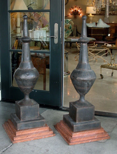 A striking and large-scaled pair of French baluster-form zinc roof finials; each tall finial with long neck above a bulbous body resting on a square plinth; all over a later faux marble wooden base