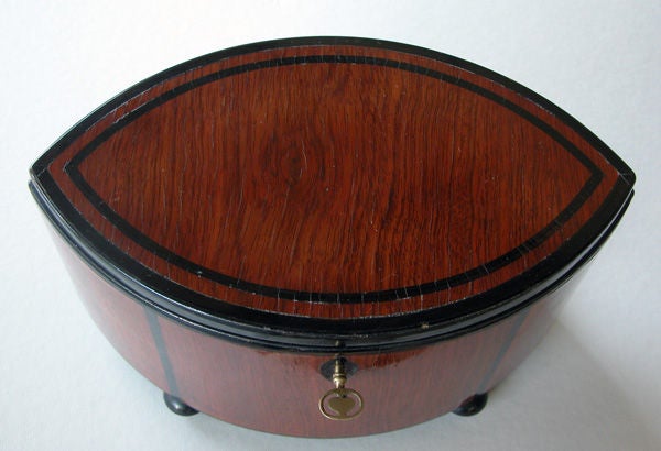 A stylish German art deco mahogany elliptical-form box with ebony inlay; the hinged elliptical lid on a conforming body all in richly-patinated and well-figured mahogany with ebony inlay; raised on 4 compressed bun feet; the interior with removable