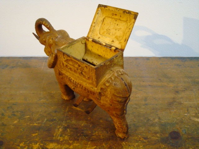 THIS FOLKY 19THC ORIGINAL PAINTED CAST IRON ELEPHANT ,WHICH LOOKS LIKE A COIN BANK ,IS A CIGARETTE DISPENSER.YOU OPEN THE  TOP LID AND TURN THE TAIL TO DISPENCE THE CIGARETTES.THE CONDITION IS VERY GOOD.