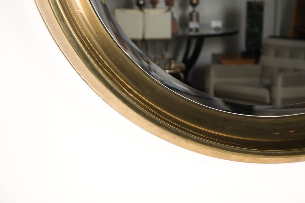 A huge porthole mirror set in a wide rimmed antique brass frame with an attenuated interior bevel. By Mastercraft. U.S.A., circa 1970.