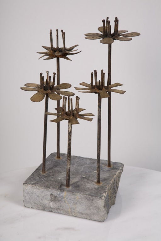 A table sculpture with candlestick functionality comprised of hand-cut abstract flowers in steel with brazed metal petals and steel pins in the center to hold candles, all supported by steel rods set in a stone base, by Curtis Jeré. American, circa