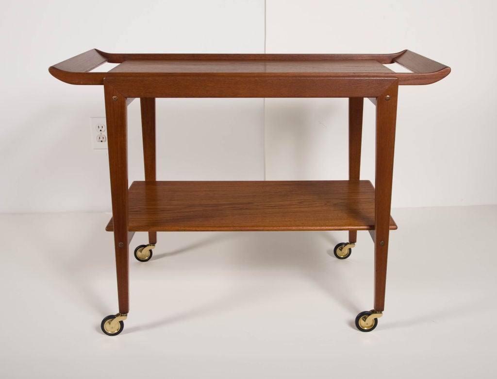 A Danish Modern teak serving tea cart with a natural oil finish, comprises a removable 'breakfast in bed' tray with upturned handles, a bottom shelf rests within square tapered legs that end in brass casters. By Tove and Edvard Kindt-Larsen.
