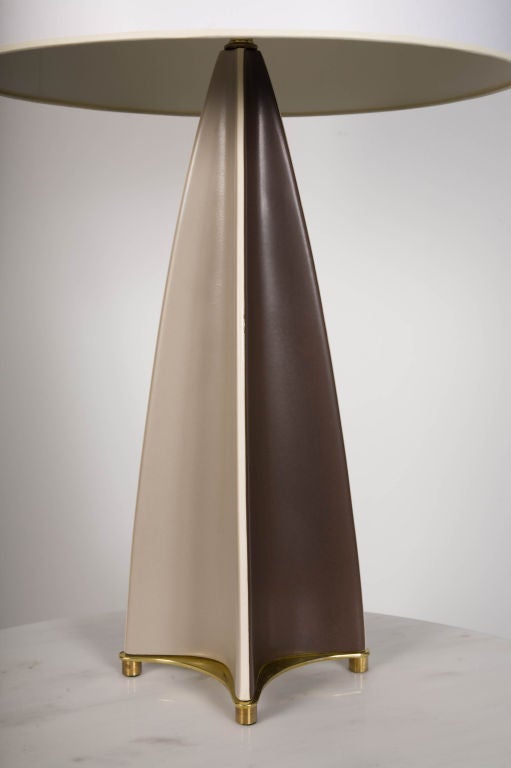 A Modernist table lamp in an elongated triangular form with concave sides glazed in a harlequin pattern of alternating colors of cream and brown. The body rests on a brass base and has a round brass finial. By Gerald Thurston for Lightolier. U.S.A.,