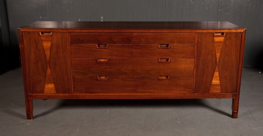 A handsome Janus gentleman’s chest in natural oiled walnut comprising four drawers each with two carved pulls flanked by doors with an elongated hourglass pattern and similar pulls that open to four drawers. Could also be used as a sideboard in the