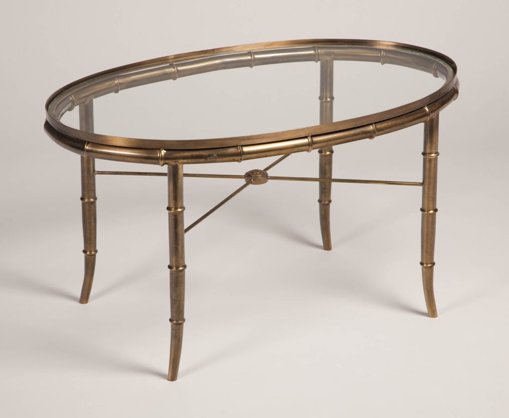 An oval cocktail table comprising a patinated brass frame in a faux bamboo form with an X-stretcher, and an inset glass top. By Mastercraft. Italian, circa 1960.