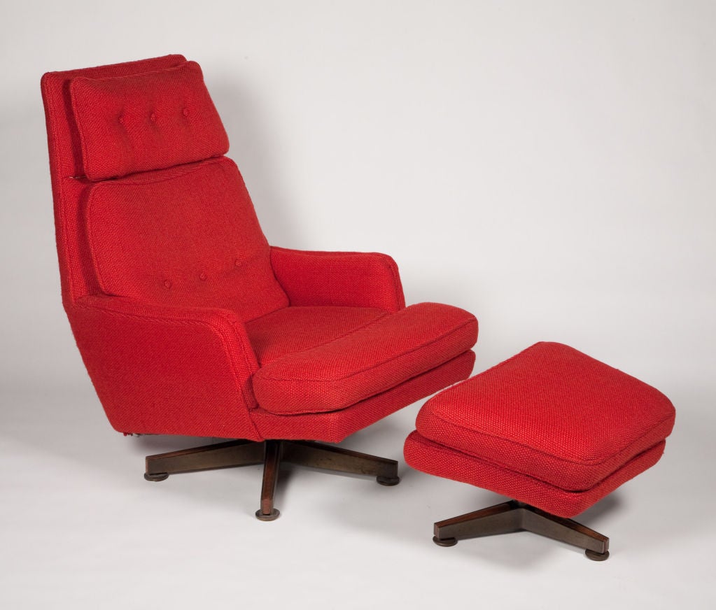 A large and comfortable lounge chair and ottoman upholstered in striking red woven upholstery. The lounge chair has two attached back cushions with button upholstery, a double cushioned seat and rests on a swiveling pedestal base. The trapezoid