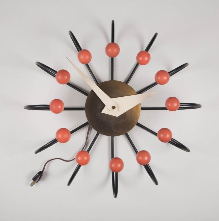 A retro Atomic Ball clock comprising a brass body with white enamel hands and black enamel arms that bend upward and inward then end in salmon lacquered wood balls.  By Frederick Weinberg. American, circa 1950.