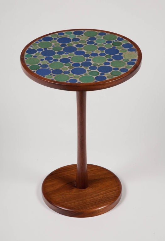 A side table with a round top inlayed with green and blue circular ceramic tiles in various sizes, the top supported by a solid walnut pedestal base. By Gordon Martz for Marshall Studios. American, circa 1950.