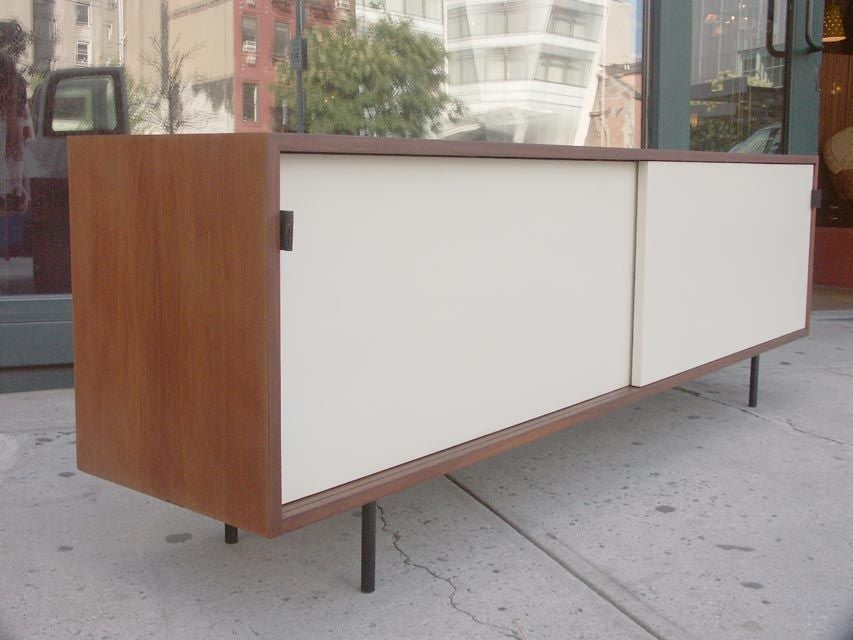 Very early example of the Knoll credenza, in walnut veneer with white sliding doors. Each door conceals a storage compartment with adjustable shelves, the right side with half depth glass shelves included. The cabinet is currently raised on low
