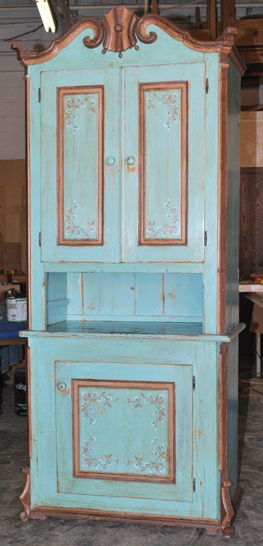 Aqua-blue cupboard in two parts with carved crown. Folk Art painted floral design adorns the door panels. 