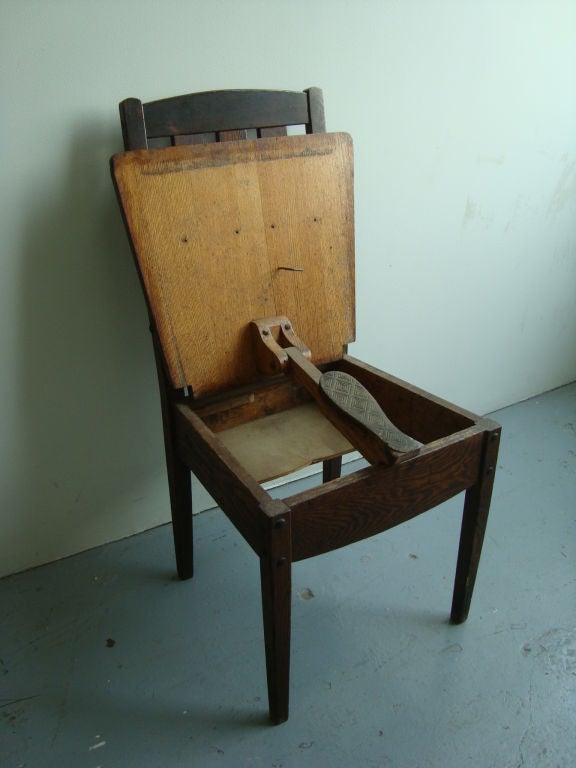 A Provincial valet shoe shine chair in rustic oak with a flap that reveals a shoe support that mechanically raises, with iron hinges.