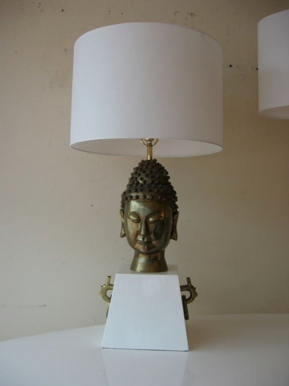 Brass Buddha lamp mounted on high gloss white lacquered base. Thick brass hoops on either side resembling earrings; Brass appointments throughout.  Sold with custom drum shade and brass finial.