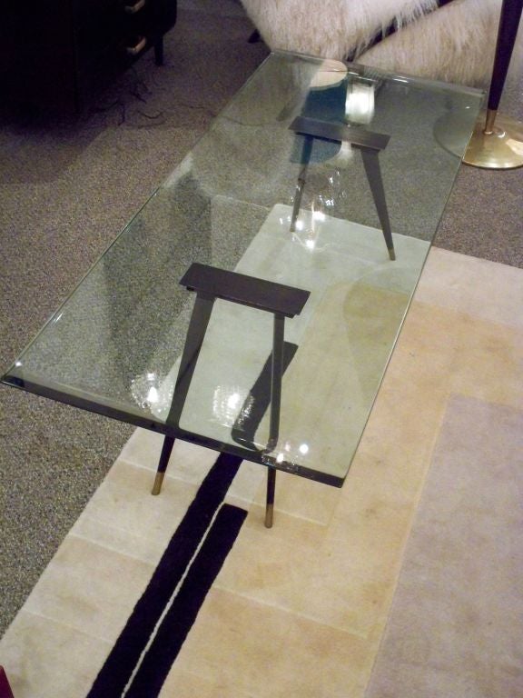 A rectangular shaped cocktail table featuring a top in thick crystal with curved reverse ground ends. The top is supported by two sets of flaring, tapering legs of black steel with brass sabots. By Max Ingrand for Fontana Arte, Italy circa 1956.