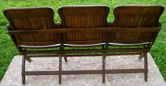 Dark brown triple seat wood slat bench. The seats lift up and fold for easy transportation. Each seat is numbered and there is a Heyward/Wakefield label attached. The bench is from an upstate NY grange hall and was also used in a grammer school