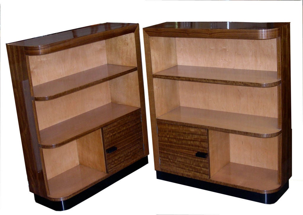 This beautiful pair of asymmetrical bookcases was designed by Gilbert Rohde and manufactured by Herman Miller in 1935. The wood is East Indian Laurelwood. They are finished in hand polished high gloss lacquer. When placed next to each other they