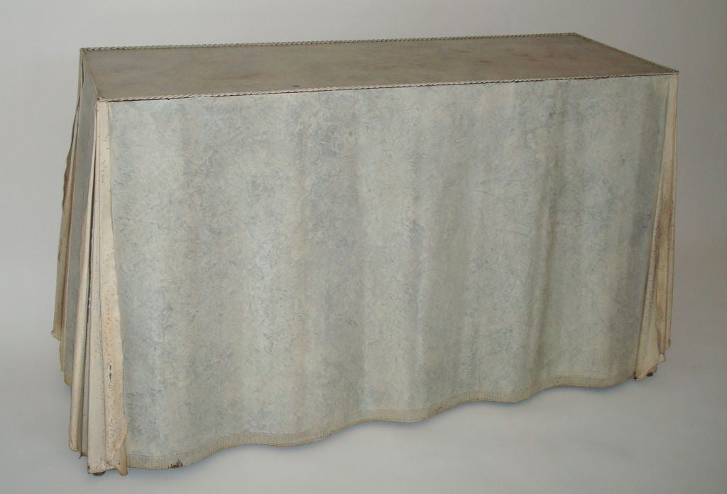 Undulating galvanized steel console table in the style of John Dickinson with flowing lightly folded fabric motif and revealed skirted edge. Stamped edge resembling fabric, rag rolled finish in light ecru, on brass feet.