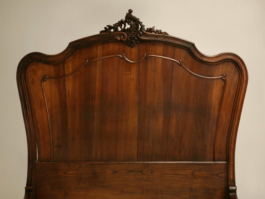Stunning antique French walnut Rococo bed with foliate scrolls, inverted seashells, and a unique flaming torch adorning the footboard, too. Outstanding details continuously draw the eye with carved, decorated, and scalloped siderails and cabriolet