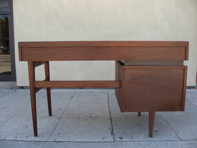 A single pedestal walnut desk from the Esprit series by Dillingham with a writing surface banded with a heavily beveled lip and two drawers all floating on an ebonized plinth style divider above a single file box size drawer.